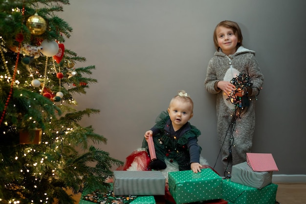 Foto kleine peuter jongen met zijn baby zus spelen in de buurt van versierde kerstboom met krans nieuwjaar