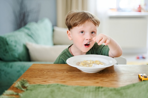 Kleine peuter kind soep eten in de keuken en zittend op de tafel