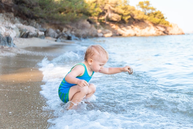 Kleine peuterjongen die zonbeschermingsbadpak draagt dat speelt met water aan de zeekant tijdens de zomervakantie in europa. kind genieten van zee. familie vakantie concept.