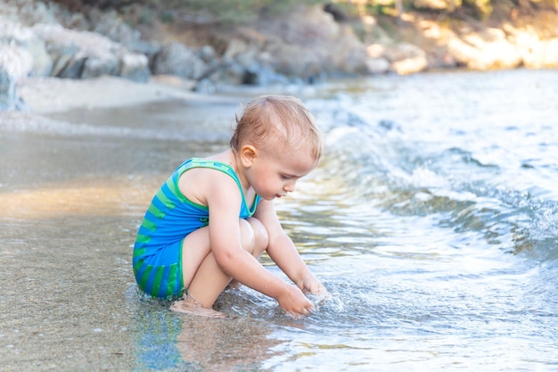 Kleine peuterjongen die zonbeschermingsbadpak draagt dat speelt met water aan de zeekant tijdens de zomervakantie in europa. kind genieten van zee. familie vakantie concept.