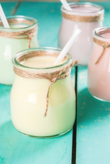 Foto kleine potten met een veelkleurige smoothie of milkshake - roze kers, paarse bes, groen en geeloranje. op een lichtblauwe houten tafel kopie ruimte