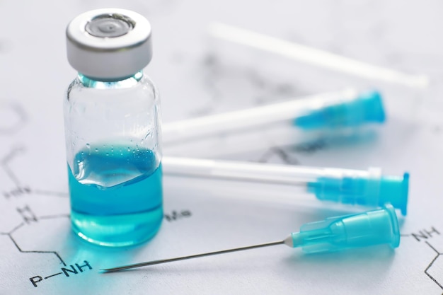 Kleine potten met injectie en spuit voor injectie op blauwe achtergrond dichtbij de chemische formule