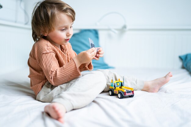 Kleine preschool jongen spelen met constructor zittend op een bed in de kamer. Kind tijd doorbrengen tijdens quarantaine. Ontwikkeling games concept, kopieer ruimte.