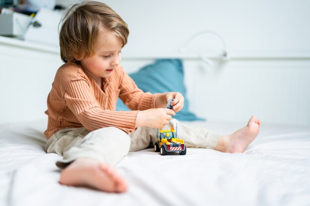 Kleine preschool jongen spelen met constructor zittend op een bed in de kamer. Kind tijd doorbrengen tijdens quarantaine. Ontwikkeling games concept, kopieer ruimte.