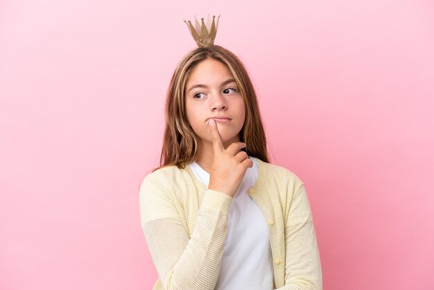 Kleine prinses met kroon geïsoleerd op roze achtergrond met twijfels tijdens het opzoeken