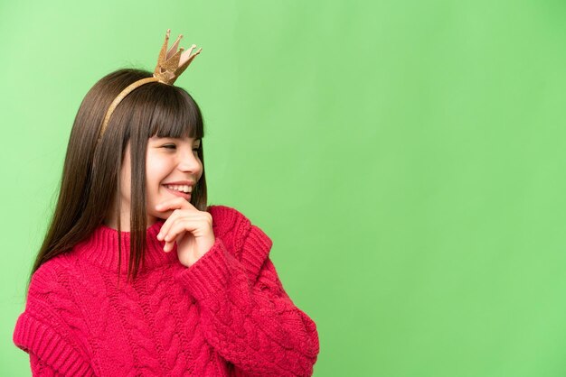 Kleine prinses met kroon over geïsoleerde chroma key achtergrond die een idee denkt en naar de kant kijkt