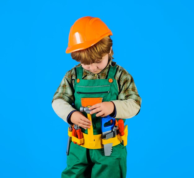 Kleine reparateur met gereedschapsriemgereedschap voor het bouwen van een bouwjongen in een veiligheidshelm en speelgoedgereedschap voor