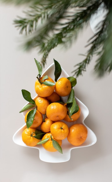 Foto kleine rijpe mandarijnen met bladeren, op plaat in de vorm van een kerstboom op beige achtergrond. concept winter vitamine voedsel. humeurige stilleven feestelijke compositie. voor wenskaart, boek, verhalen.