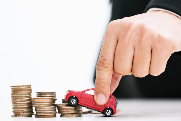 Kleine rode auto over heel wat geld gestapelde muntstukken. Voor leningen kost het concept financieren.