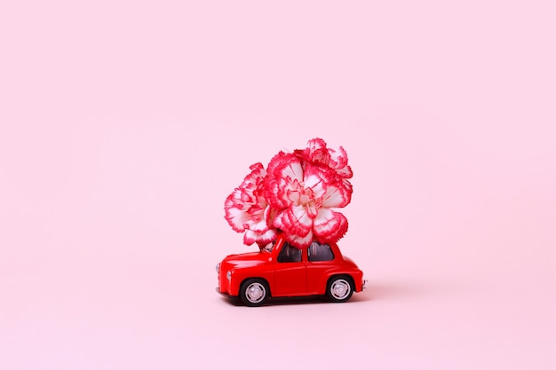 Kleine rode retro speelgoedauto met bloem op het dak Levering van cadeaus voor Valentijnsdag Wereld Womens Day