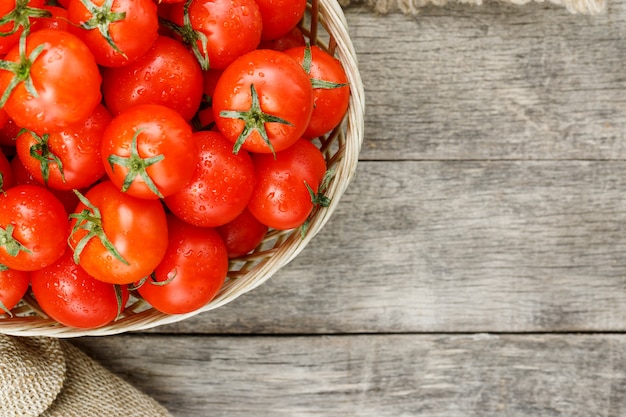 Kleine rode tomaten in een rieten mand op een oude houten tafel. Rijpe en sappige kers