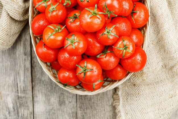 Kleine rode tomaten in een rieten mand op een oude houten tafel. rijpe en sappige kers