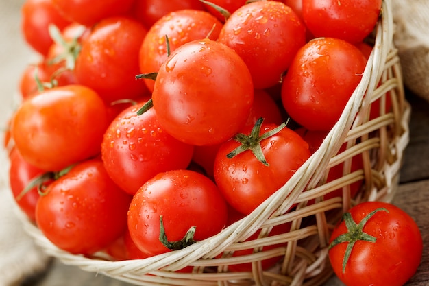 Kleine rode tomaten in een rieten mand op een oude houten tafel. rijpe en sappige kers