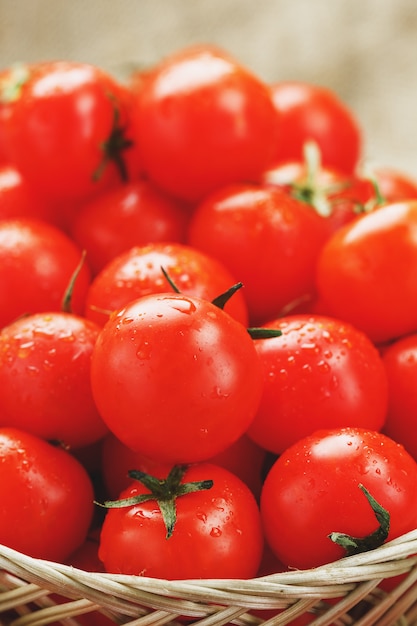 Kleine rode tomaten in een rieten mand op een oude houten tafel. Rijpe en sappige kers