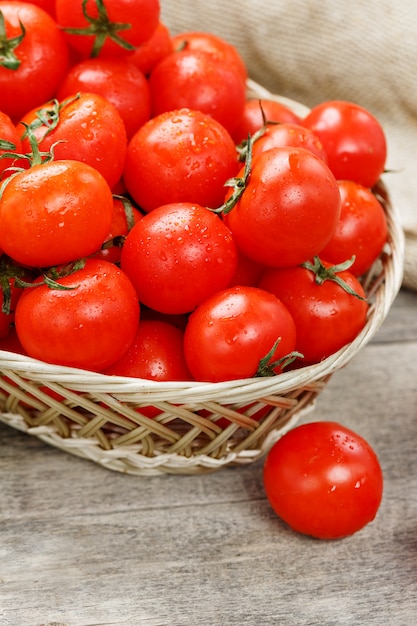 Kleine rode tomaten in een rieten mand op een oude houten tafel. Rijpe en sappige kers