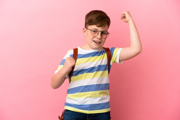 Kleine roodharige blanke jongen geïsoleerd op roze achtergrond die een overwinning viert