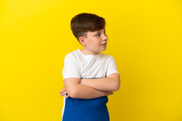 Kleine roodharige jongen geïsoleerd op geel oppervlak kijkend naar de zijkant