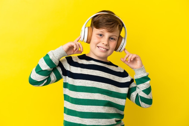 Kleine roodharige jongen geïsoleerd op gele achtergrond muziek luisteren en zingen