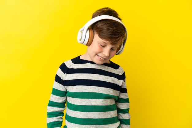 Kleine roodharige jongen geïsoleerd op gele muur luisteren muziek