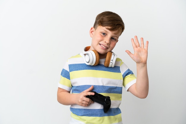 Kleine roodharige jongen met een gamepad geïsoleerd op een witte achtergrond saluerend met de hand met gelukkige uitdrukking