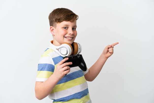 Kleine roodharige jongen met een gamepad geïsoleerd op een witte achtergrond, wijzend met de vinger naar de zijkant en een product presenterend