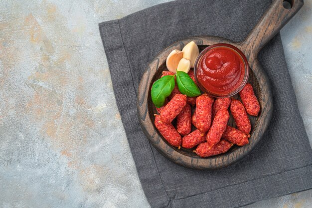 Kleine rookworstjes, knoflook, ketchup en basilicum, op een grijs bureau met een servet. Bovenaanzicht met kopie ruimte.