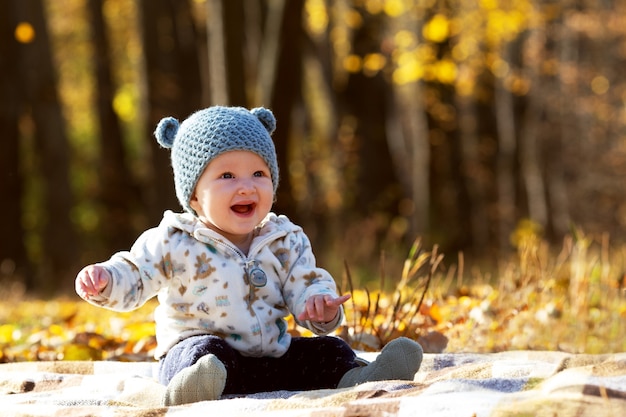 Kleine schattige baby in grappige hoed met oren en hoody zittend in het park op zonnige herfstdag
