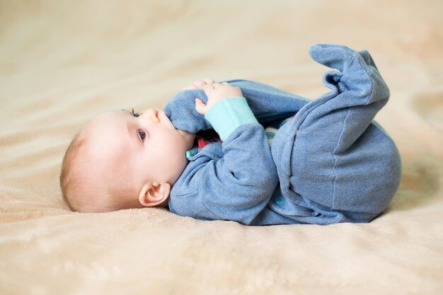 Kleine schattige baby in schattige blauwe bommenwerper bijt in zijn voet op bed