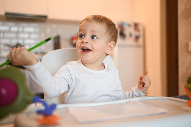 Kleine schattige baby peuter jongen blonde zittend op de kinderstoel leren tekenen met kleurpotloden baby