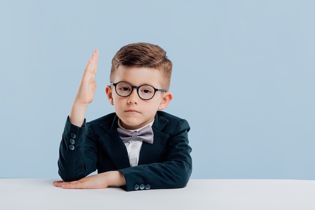 Kleine schattige jongen draagt een bril en een zwart pak