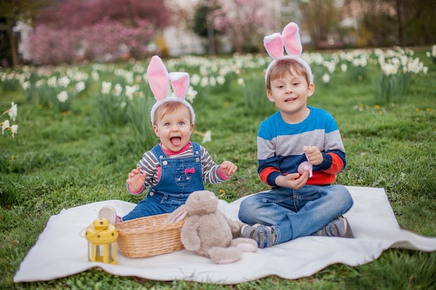 Kleine schattige jongen en meisje zitten op het gras in de buurt van de narcissen