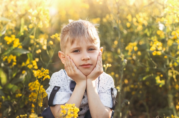 Kleine schattige jongen in een koolzaadveld. Landelijk landschap.