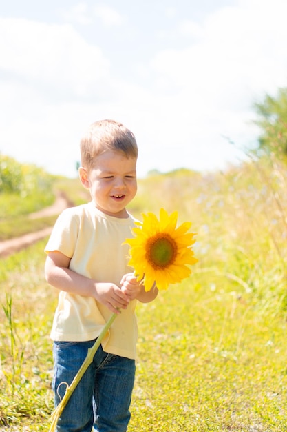 Kleine schattige jongen in een veld met zonnebloemen in een geel t-shirt staat en glimlacht