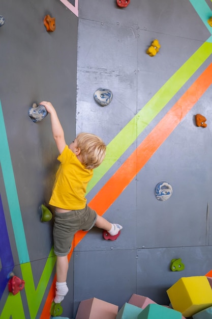 Kleine schattige jongen klimt op verticale muur binnen in amusementspark