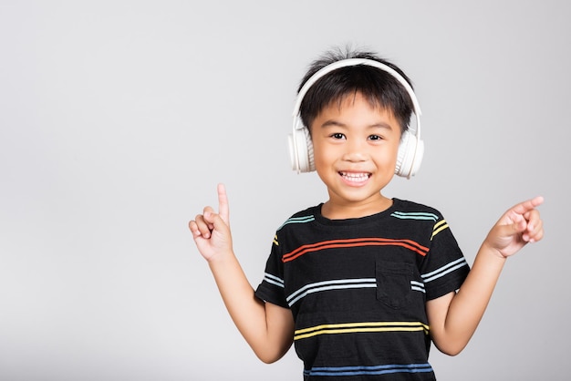 Kleine schattige jongen van 5 jaar oud luistert naar muziek in een draadloze koptelefoon