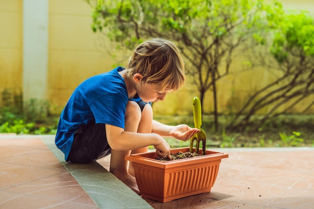 Kleine schattige jongen zaait zaden in een bloempot in de tuin