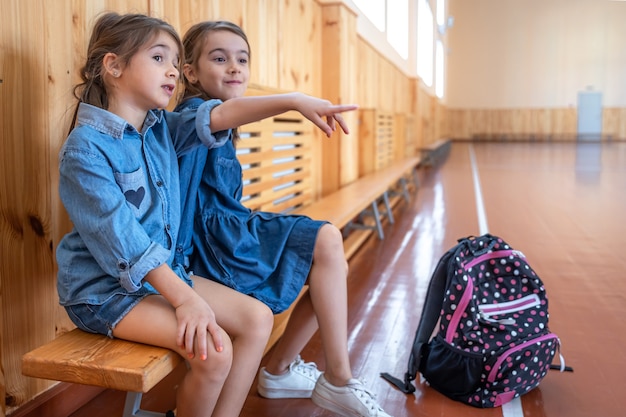 Kleine schattige meisjes, basisschoolmeisjes, met rugzakken na school in een lege schoolgymnastiek.