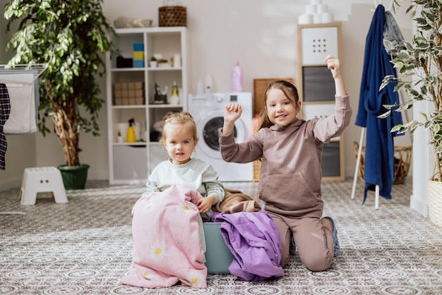 Kleine schattige meisjes die in de wasruimte zitten, het blonde meisje speelt in een kom met kleren