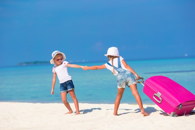 Kleine schattige meisjes met grote koffer op tropisch wit strand