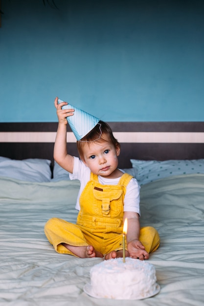 Kleine schattige peuter viert haar verjaardag thuis op bed met taart