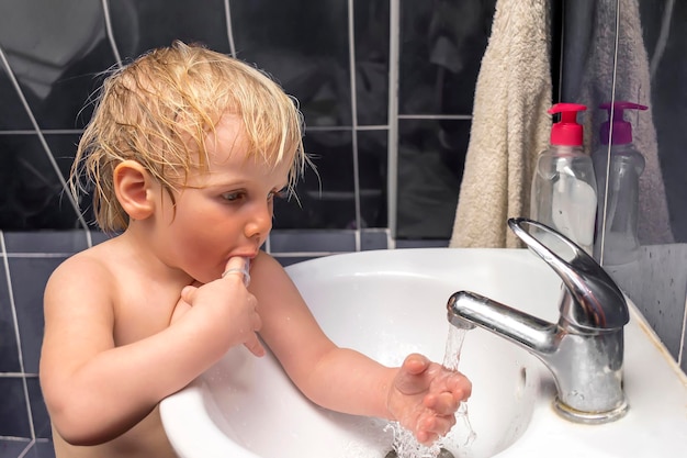 Kleine schattige schattige blonde blanke babyjongen handen wassen en tanden poetsen met tandenborstel thuis in de ochtendavond grappig kind doet dagelijkse hygiëne gezondheidszorg