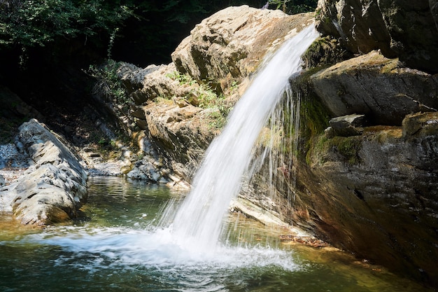 Kleine schone waterval valt van een rotsachtige richel in een beboste bergvallei