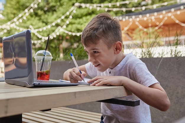 Kleine schooljongen huiswerk buitenshuis met laptop schrijven van notities in beurt