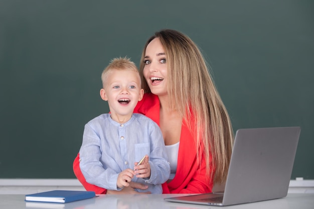 Kleine schoolkindzoon die laptop gebruikt met een moederleraar die schoolkind helpt in de klas op scho