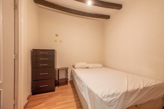 Kleine slaapkamer met balkenplafond, queensize uitschuifbed, bruine ladekast, toegang tot een badkamer en houten vloer