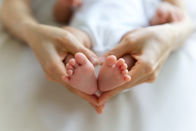 Kleine slapende baby voeten in handen van de moeder. Moederhanden die de voeten in hartvorm houden.