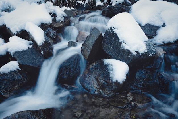 Kleine snelle stroom tussen kleine natte stenen en koude witte sneeuw in de pittoreske Karpaten in het prachtige Oekraïne en zijn fantastische natuur