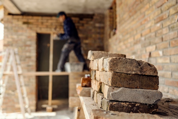 Foto kleine stapel stenen op een bouwplaats met een arbeider op de achtergrond die een huis bouwt