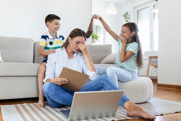 Kleine stoute kinderen die de drukke jonge vrouw afleiden van het werk op de laptop thuis