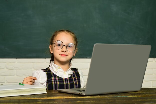 Kleine student leerling met laptop. Concept van onderwijs en lezen. Kind is klaar om te antwoorden met een schoolbord op een achtergrond.